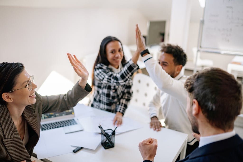 A diverse group of colleagues celebrating success in a bright office setting with high fives.